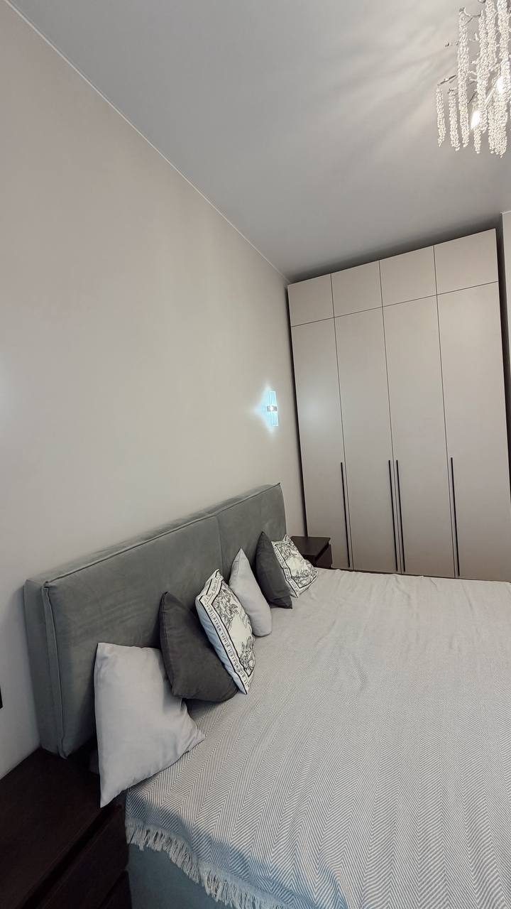 Спальня в ЖК Остров: кровать с мягким изголовьем, покрывало и подушки, белый шкаф до потолка
